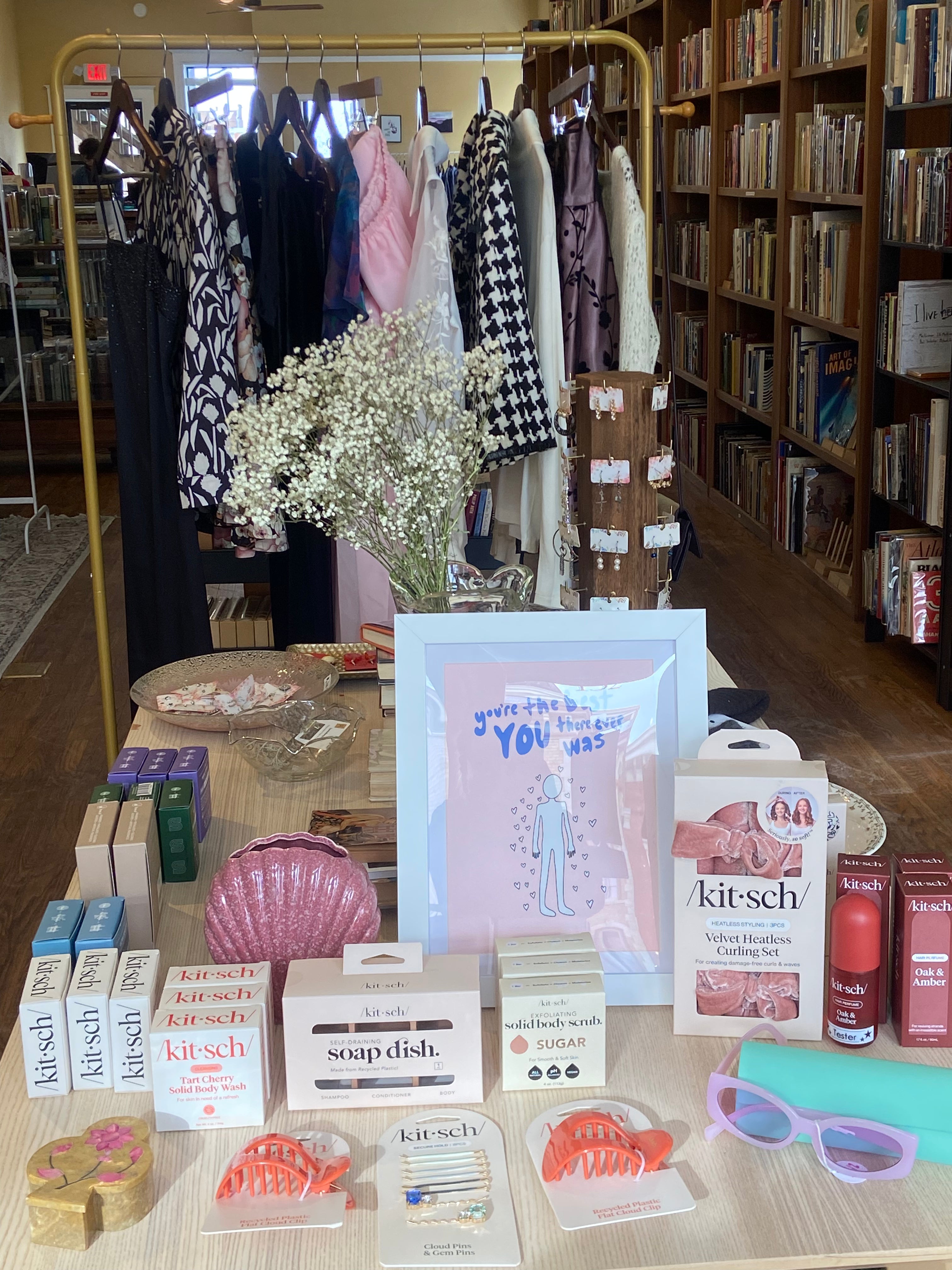 A retail display featuring Kitsch hair products, vintage home decor, clothing, and purple sunglasses